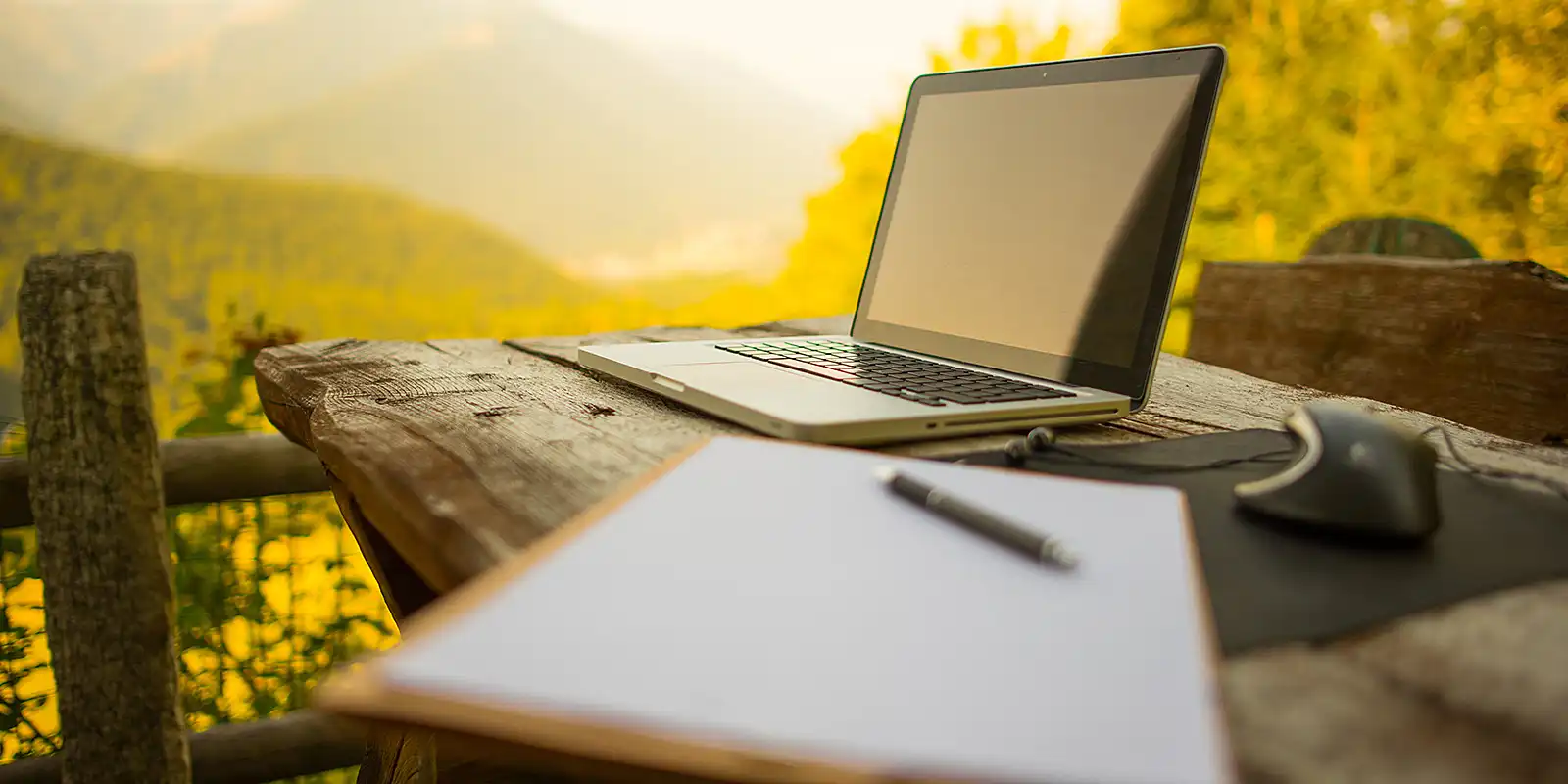 A laptop computer standing on a wooden table at sunset.